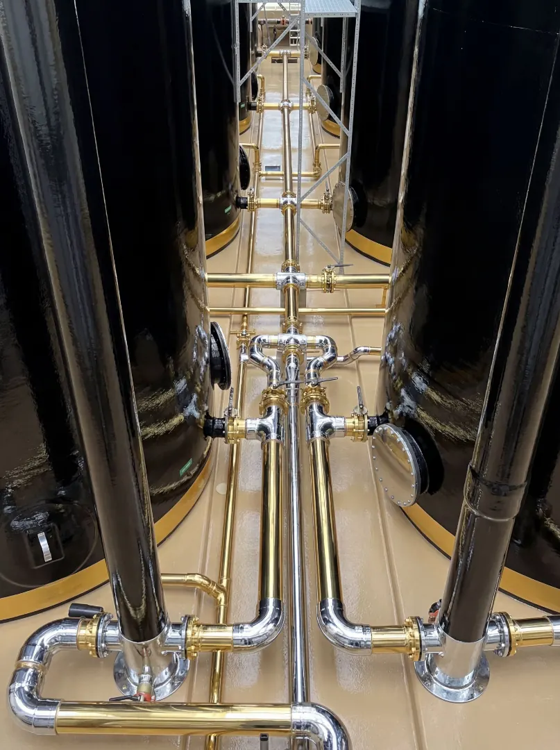 Vertical view of a polished piping manifold between black storage tanks