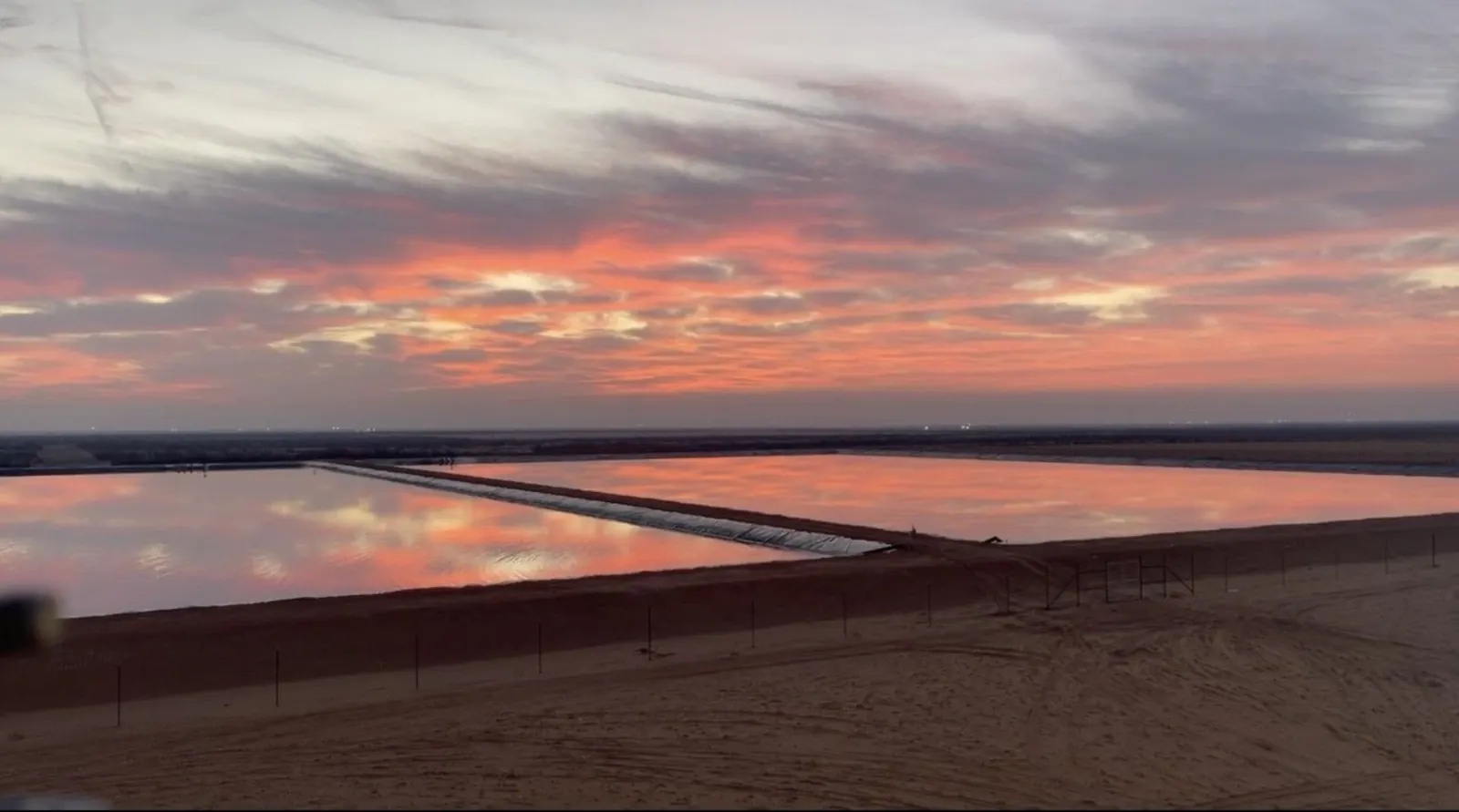 Large water-storage ponds reflecting a West Texas sunset